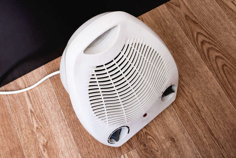 Compact electric heater placed on a wooden floor near a wall. - electric heater vs central heating