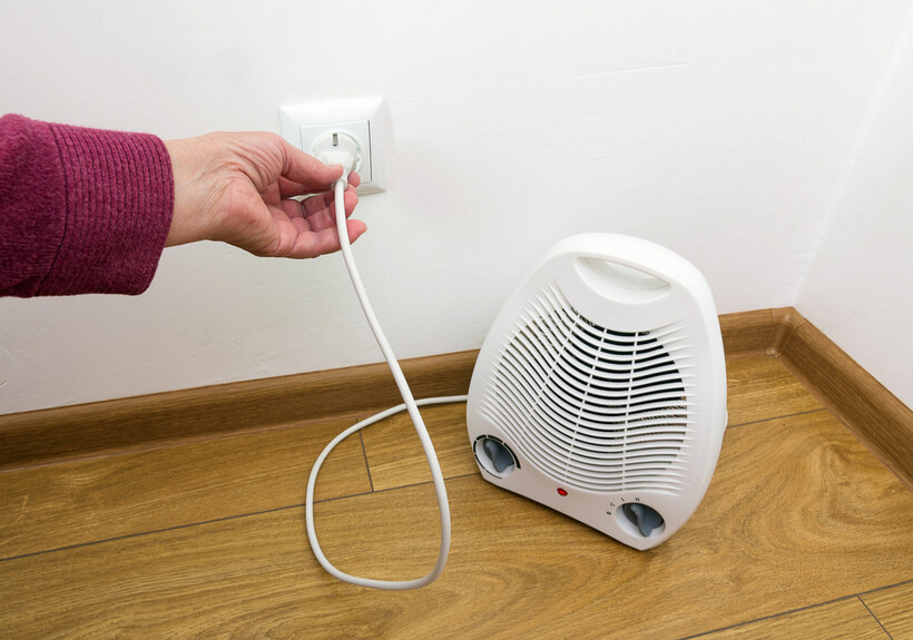 Person plugging in an electric heater to a wall outlet on a wooden floor. - electric heater vs central heating