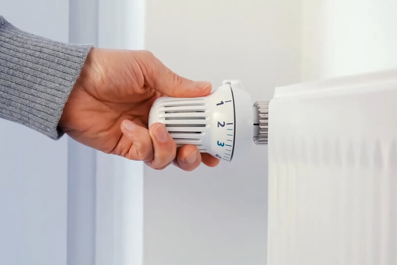 Hand adjusting a radiator thermostat connected to a central heating system. - central heating vs electric heater