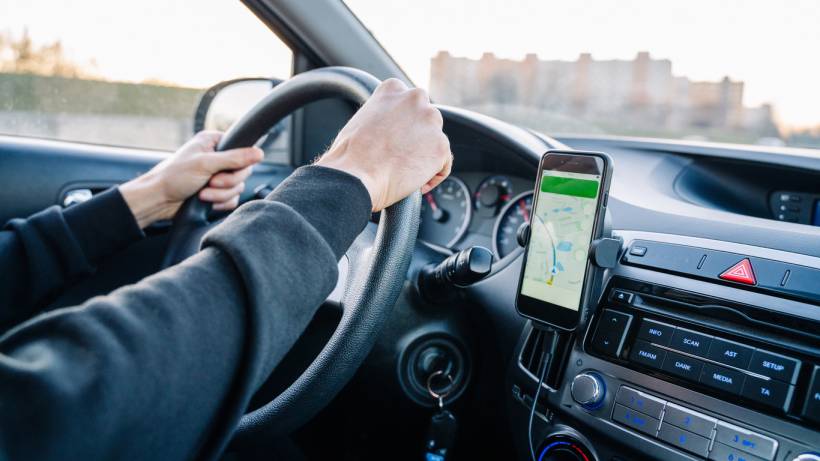 A person using a navigation app on a mobile phone while driving a car. - make money with your car