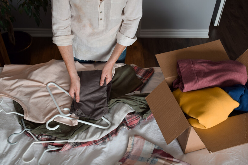 Person sorting clothes on a bed next to a box during a declutter process. - last minute moving