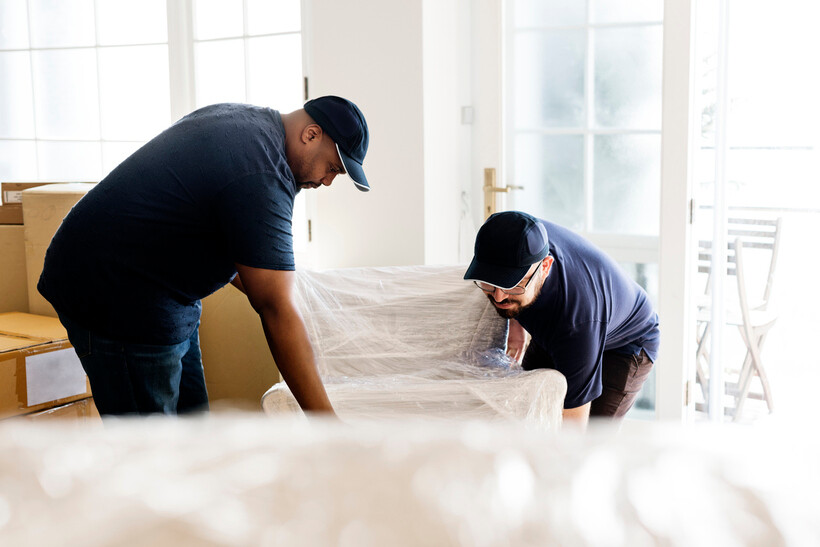 Two professional removalists lifting a wrapped armchair. - moving stress