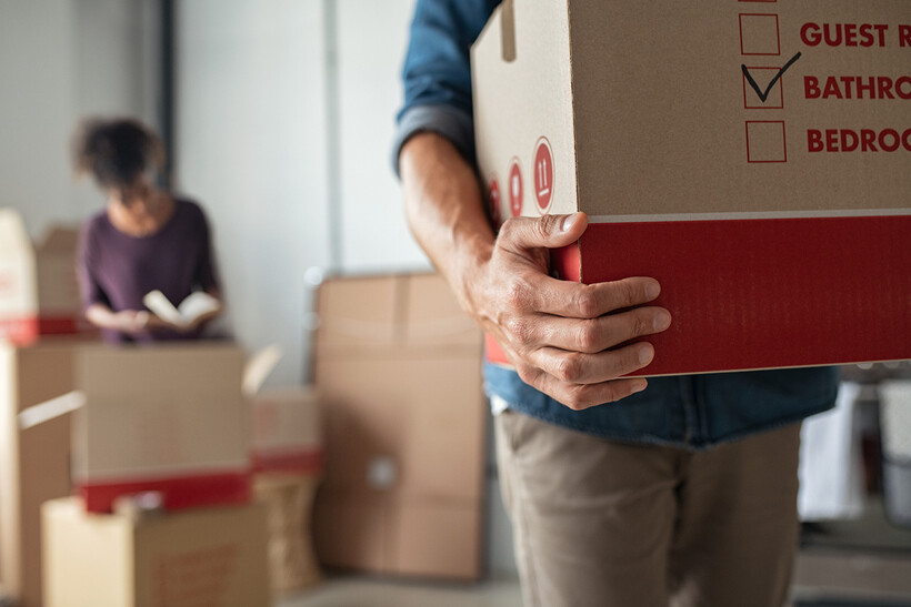 Man holding a bathroom-labelled box while unpacking in a new home. - moving stress