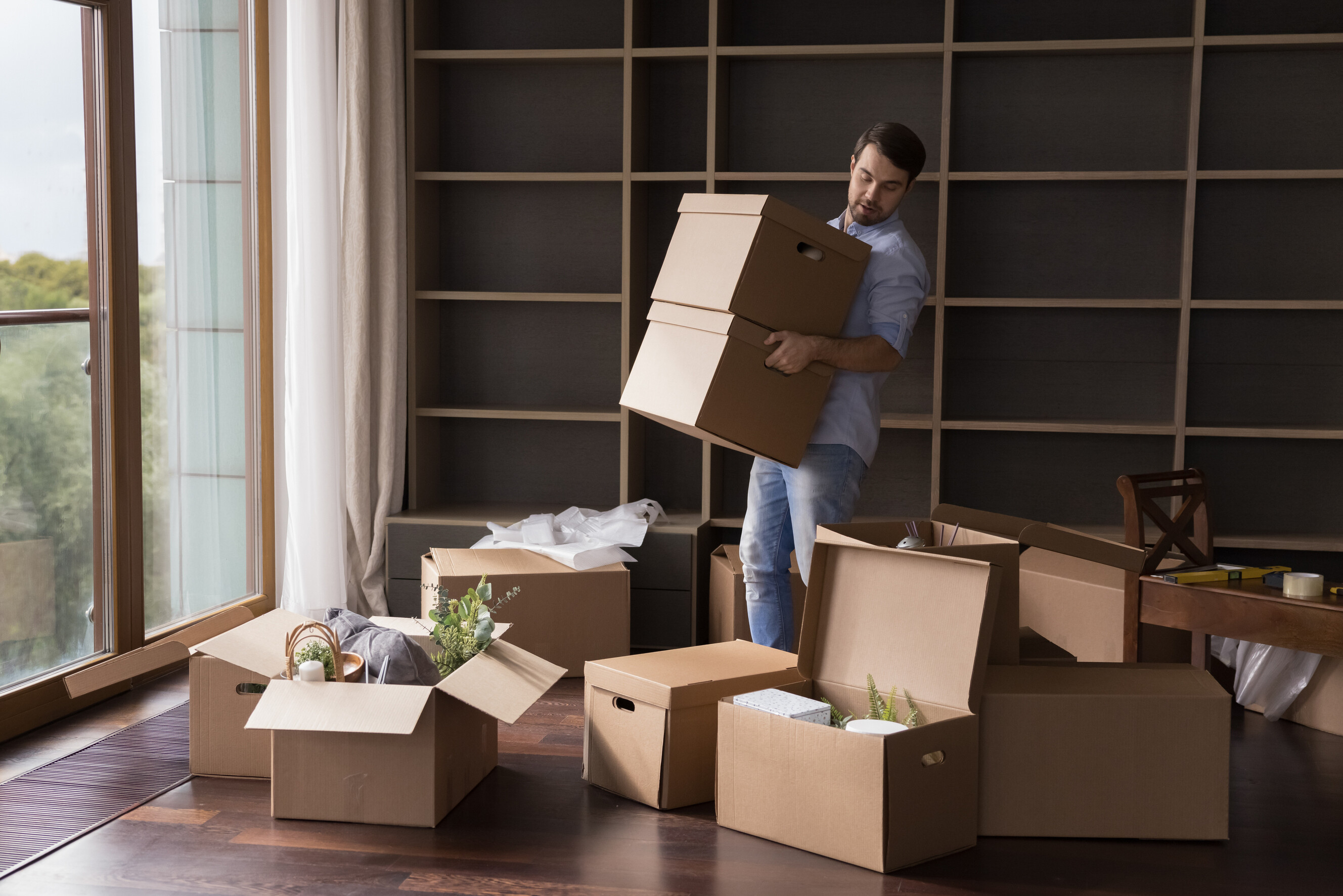 Man carrying cardboard boxes in an empty living room during a DIY home move.