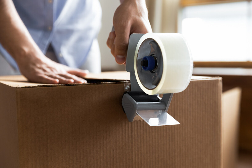 Close-up of person sealing a moving box with packing tape dispenser. - DIY moving