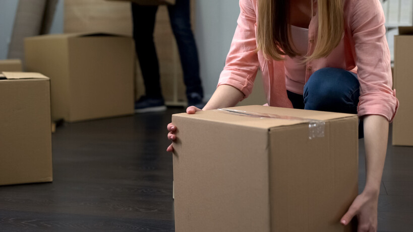 Close-up of person handling moving box on dark wooden floor. - DIY moving