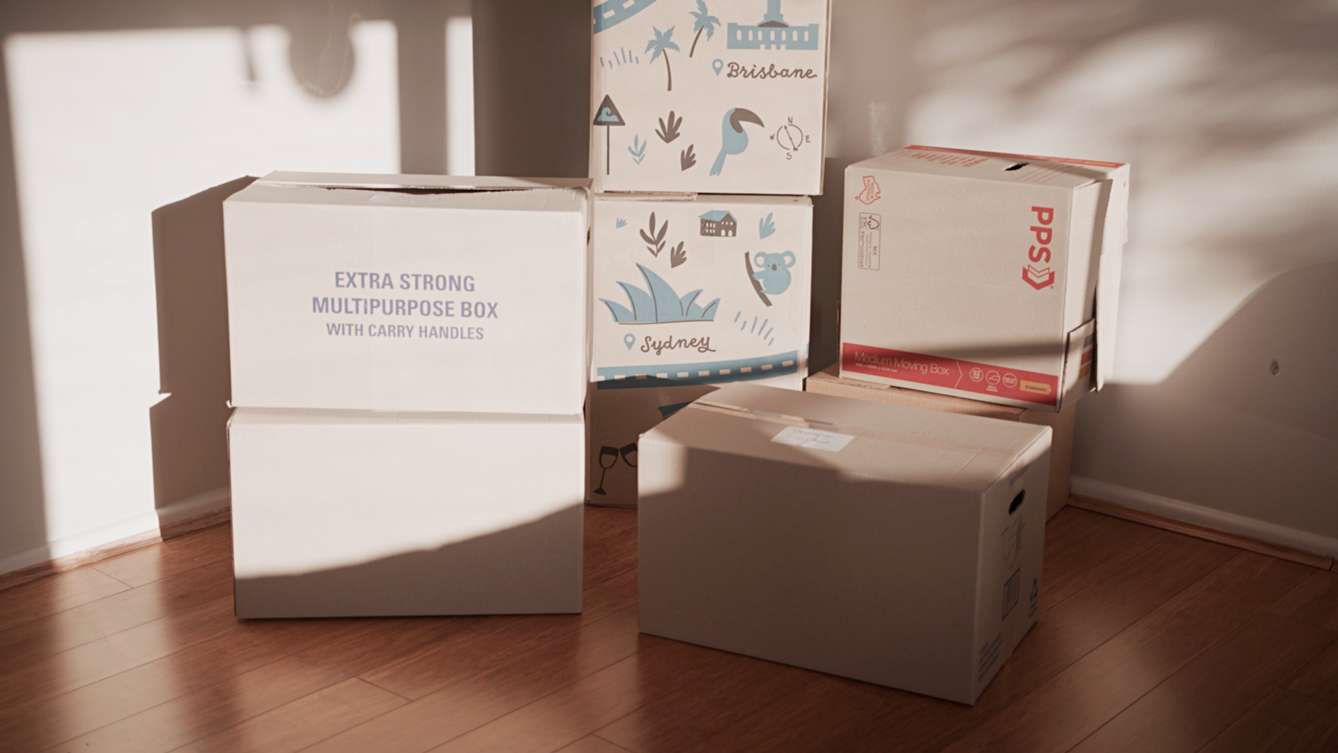 house removals cost - Various moving boxes with printed designs and labels placed near a wall