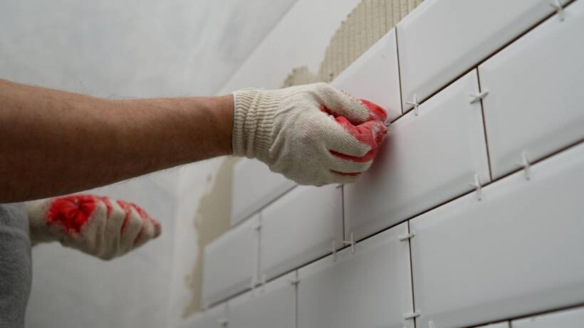 close-up of gloved hand setting ceramic subway tile with spacers - how to tile a wall