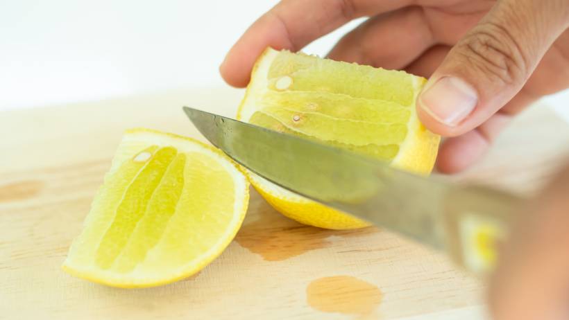 slicing a fresh yellow lemon into wedges on a wooden cutting board - descaling a kettle