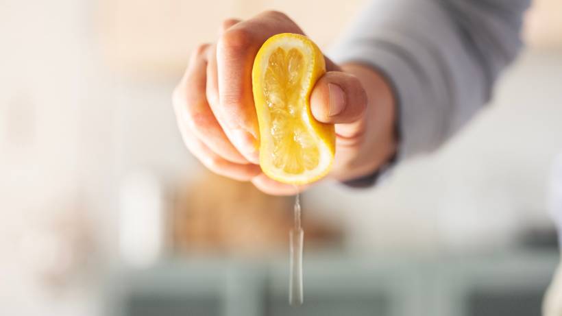 Hand squeezing a halved yellow lemon to extract juice - how to descale kettle
