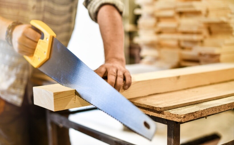 DIY loft bed - Carpenter sawing timber with a yellow-handled saw.