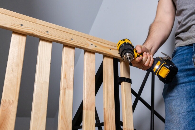 DIY loft bed - Person holding a cordless drill near a wooden bed rail.