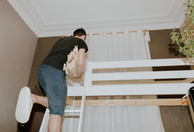 DIY loft bed - Person climbing ladder while holding wooden slats near a loft bed.
