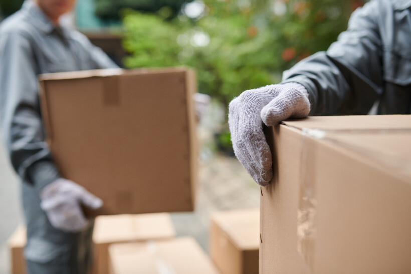Close-up of gloved hands carrying moving boxes outdoors. - moving mistakes