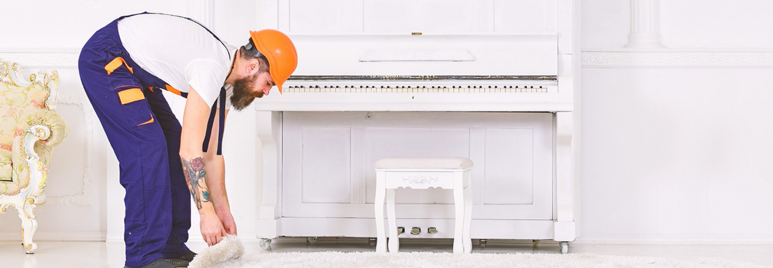 A piano removalist preparing to move an upright piano in a home, lifting a rug to make space for safe piano transport.
