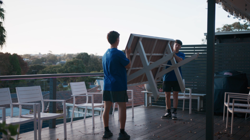 Two people in blue shirts moving a large outdoor table on a wooden deck. - moving guide