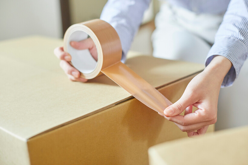 A woman securely sealing a moving box in a living room setting. - packing tape vs duct tape