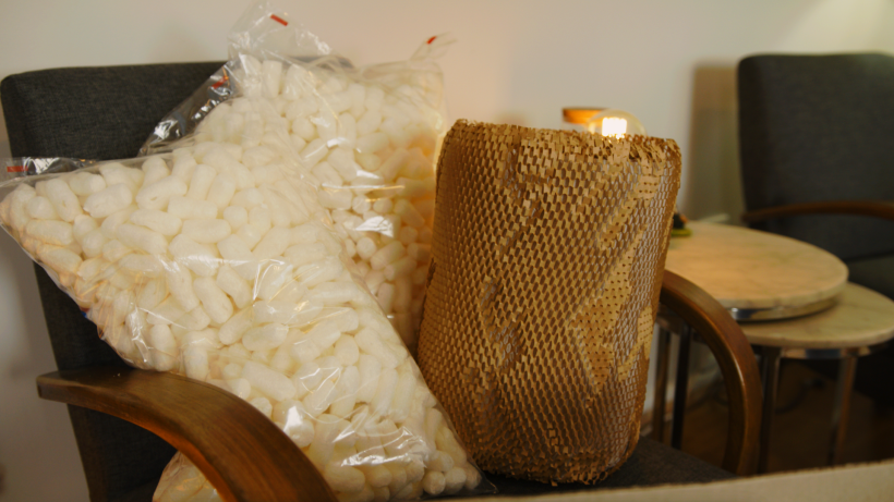 Bags of white packing peanuts and a roll of honeycomb paper wrap on a chair. - how to pack small appliances