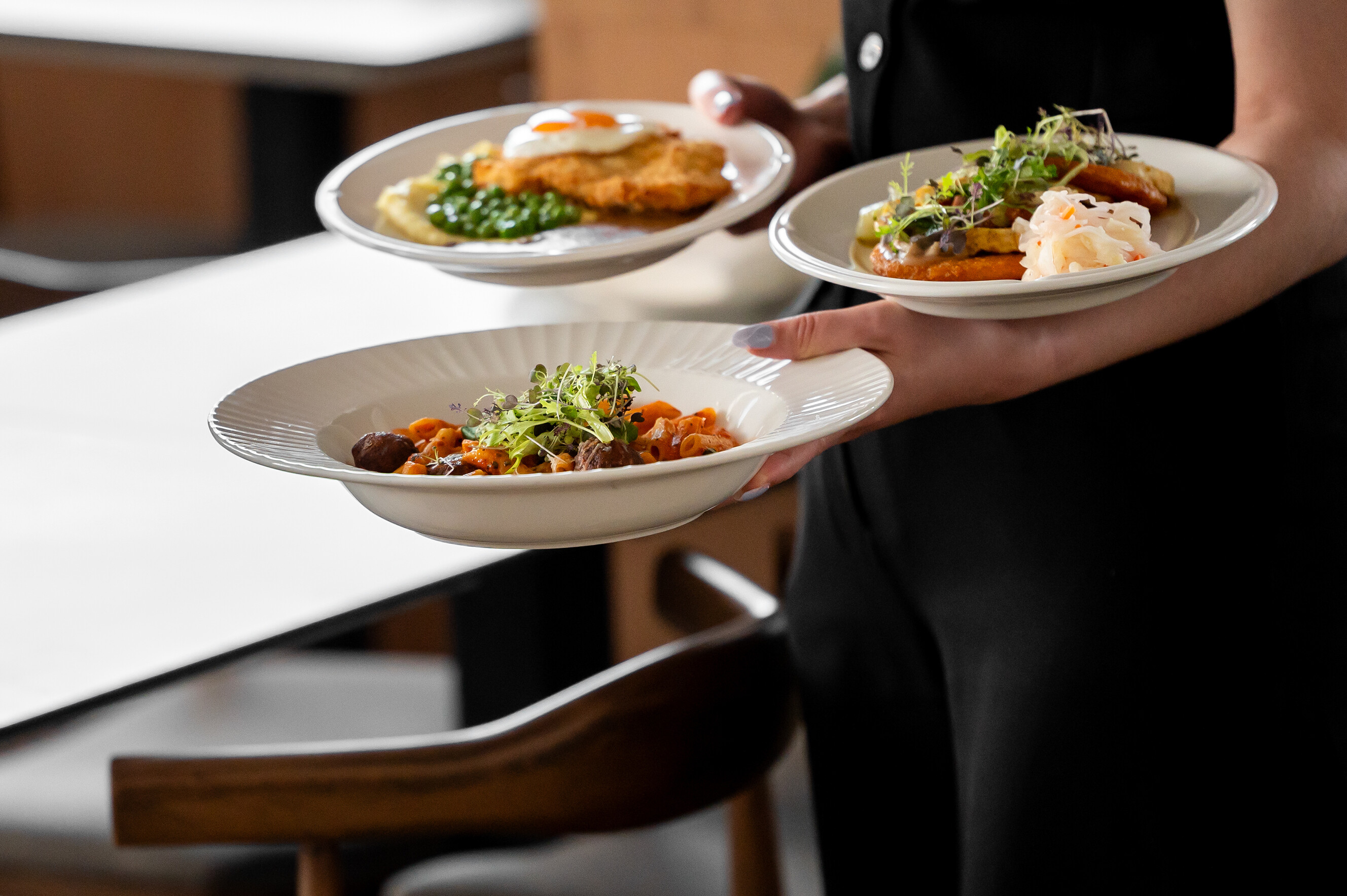 Close up of a wait staff carrying three high-quality plates of pasta for a seated dinner.