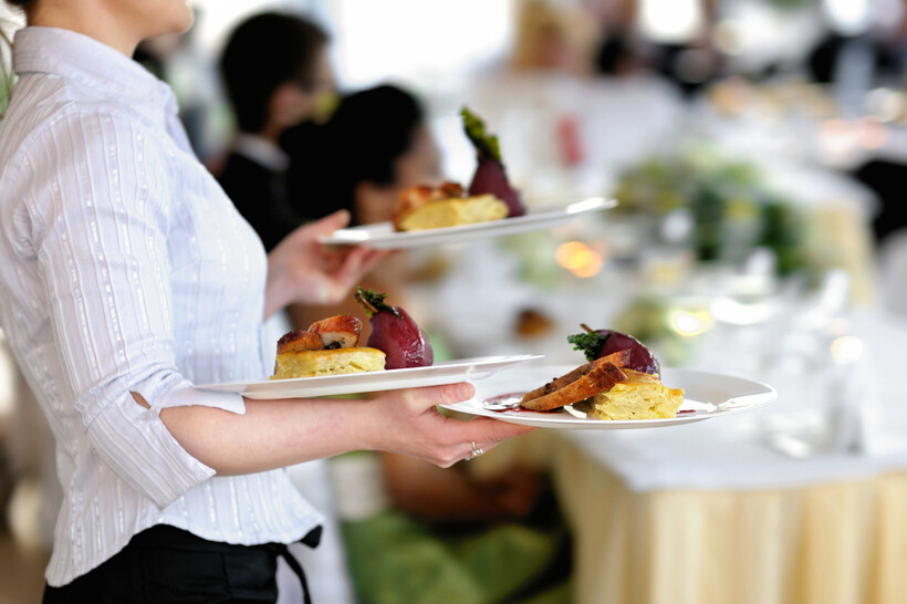 Professional server delivering pre-plated courses to a table during a formal event. - plated vs buffet