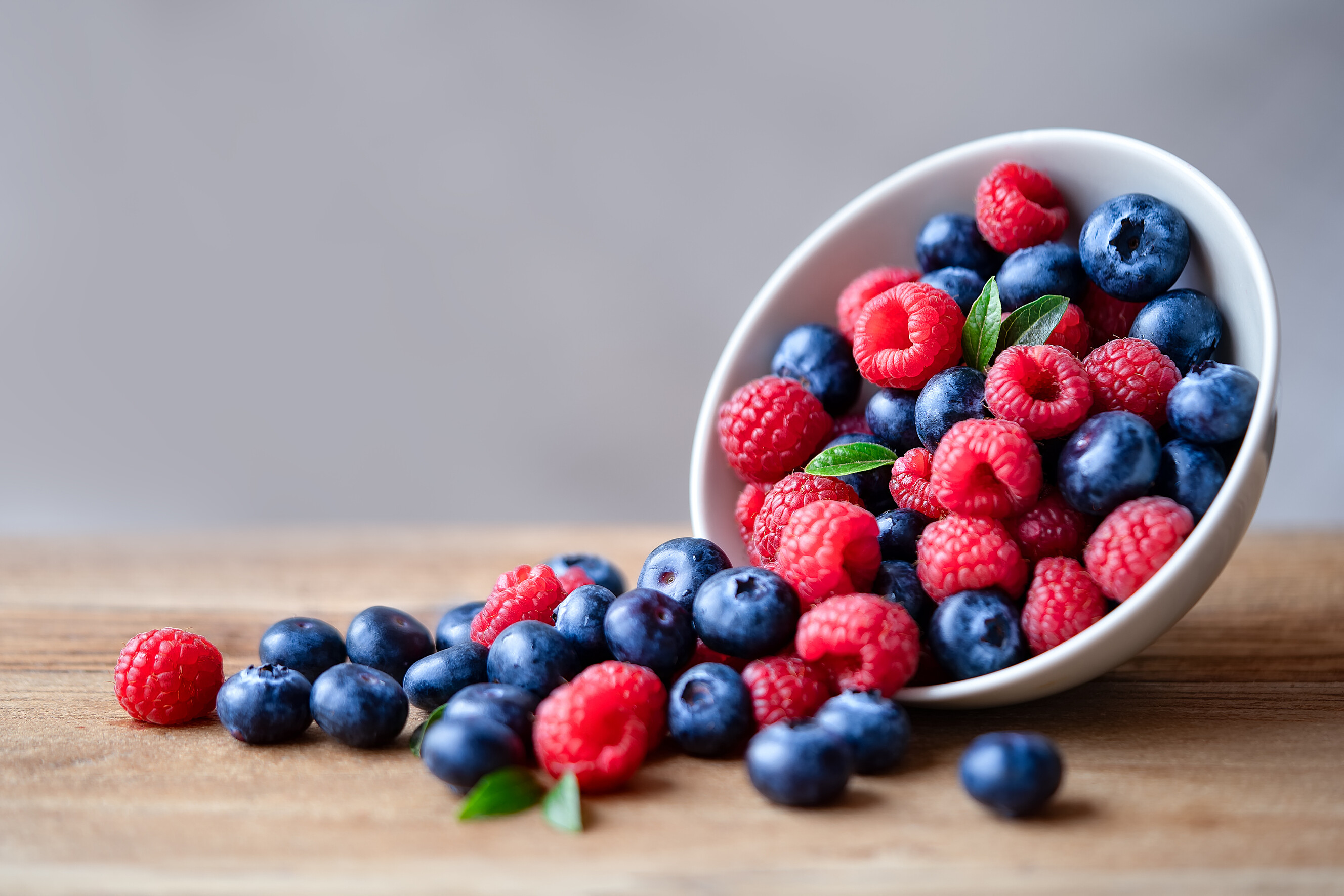 Clustered raspberries and smooth blueberries displayed together on a wooden surface.