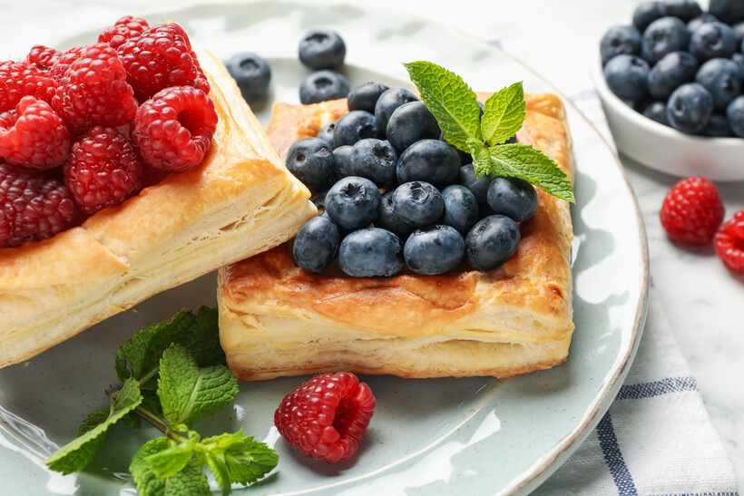 Delicious puff pastries topped with fresh berries and mint leaves on a white table. - raspberry vs blueberry