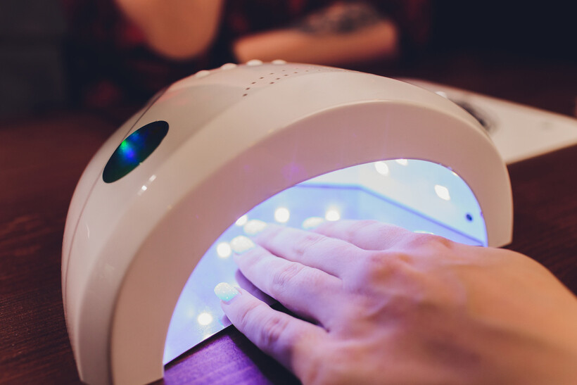 A hand placed inside a professional UV nail lamp to cure multiple layers of gel. - gel nail extensions vs acrylic