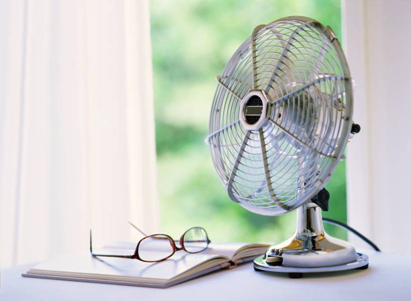 fan vs air conditioner - Retro-style table fan beside reading materials in a softly lit room