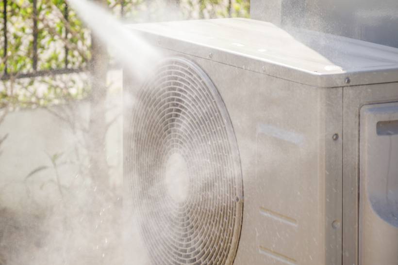 fan vs air conditioner - Outdoor AC unit being cleaned with a high-pressure water spray
