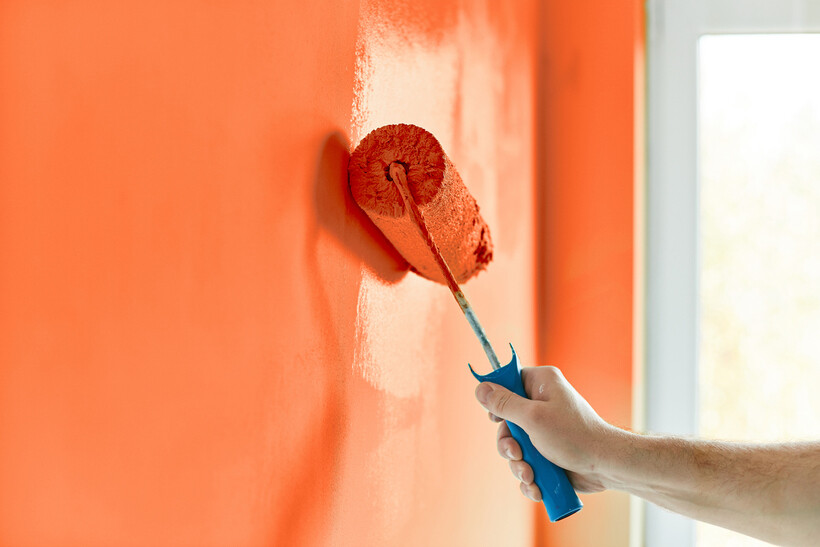 Close-up of a person using a paint roller to apply orange paint to an apartment wall. - wallpaper vs paint