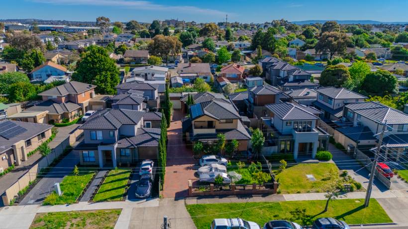 Aerial view of modern multi-story townhouses in Melbourne featuring dark tiled roofs, paved driveways, and landscaped front yards in a suburban neighbourhood. - moving to melbourne