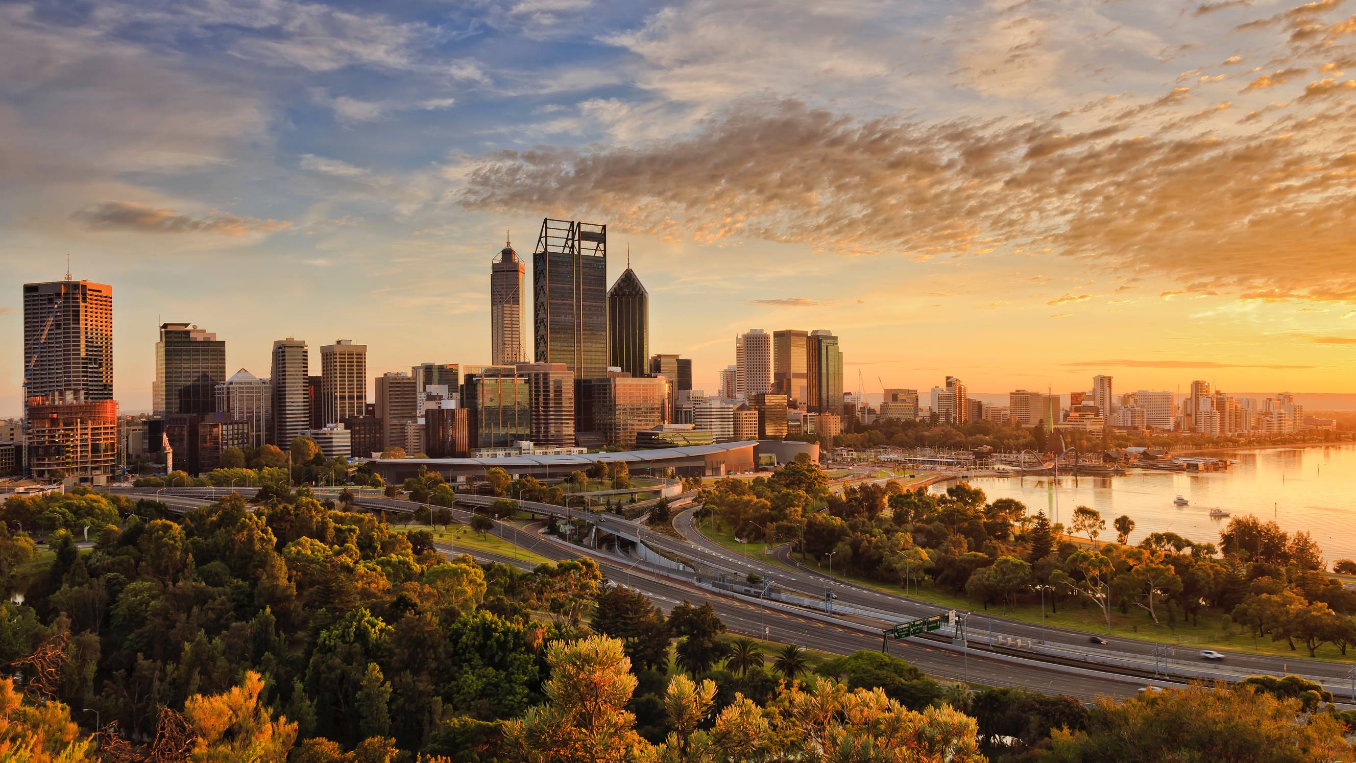 Panoramic view of the Perth cityscape from Kings Park at sunset, featuring the Central Business District skyline, Swan River, and lush greenery in the foreground.
