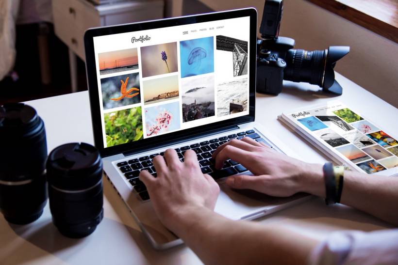 how to make money with photography - Photographer reviewing an online photo portfolio at a desk with lenses and a DSLR camera