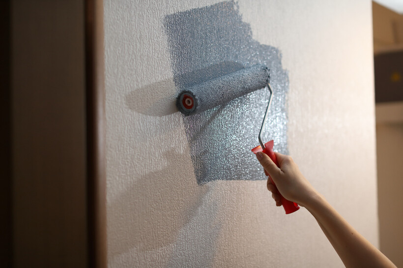Hand using a paint roller to apply satin gray paint to an interior wall. - satin vs gloss paint