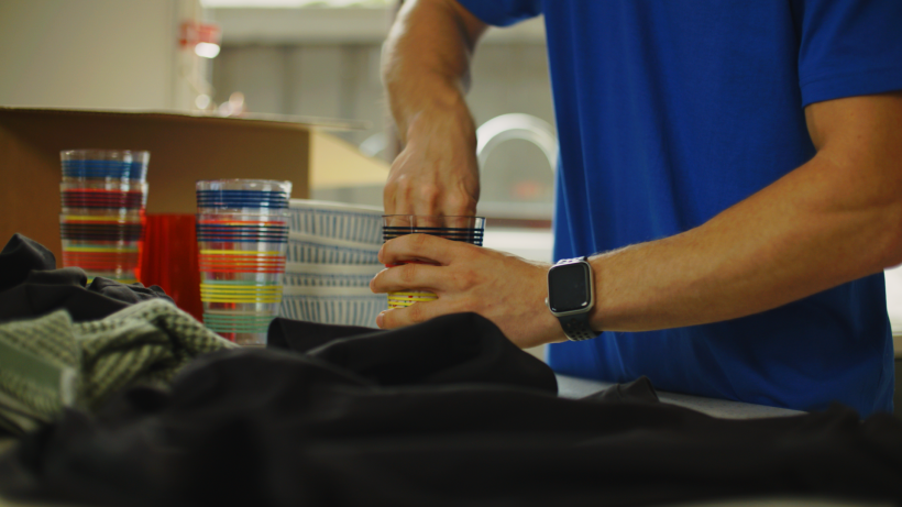 Close-up of hands handling striped glassware on a kitchen counter with protective clothing and boxes in the background. - how to pack glasses for moving