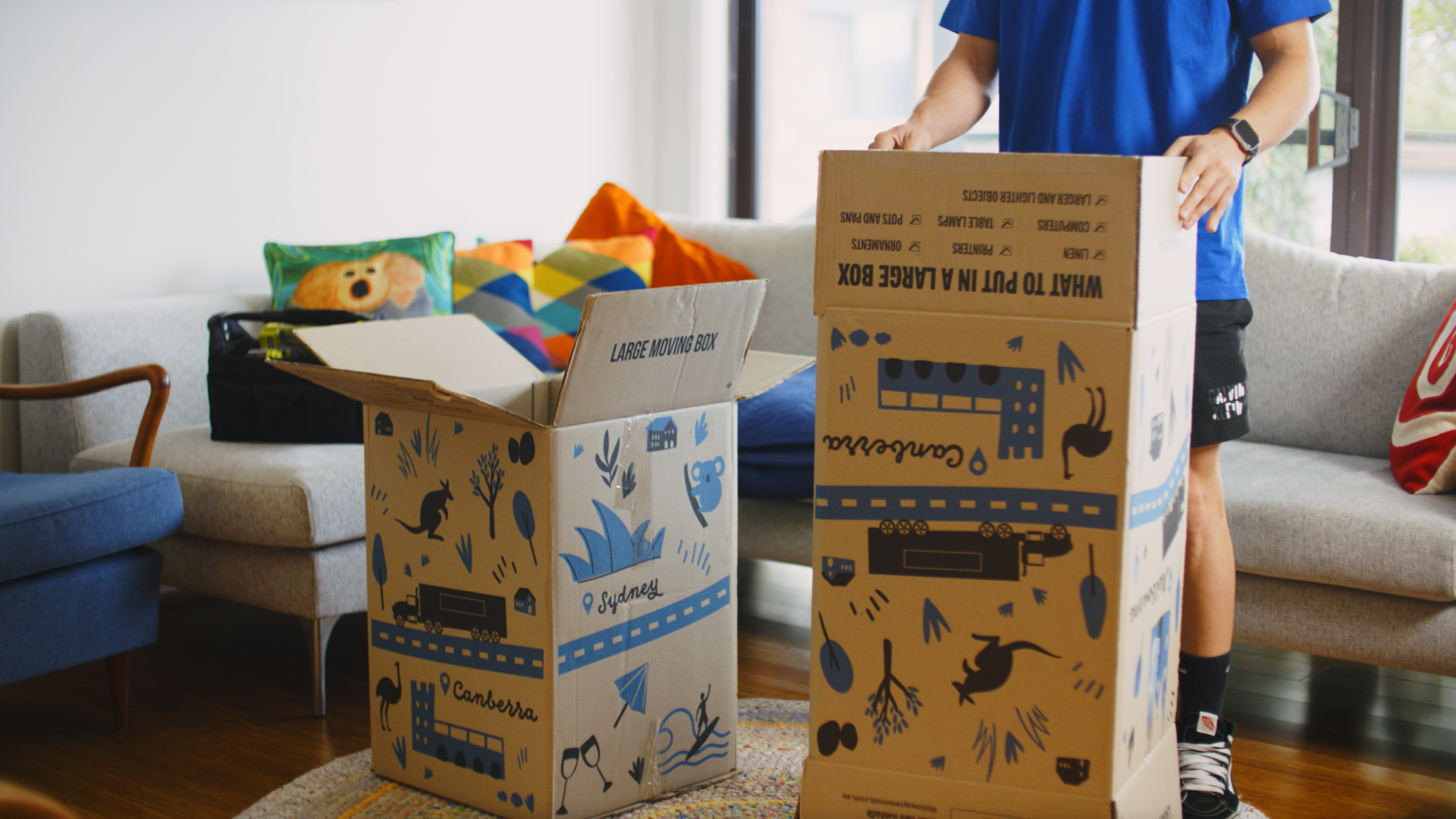 Moving house with large cardboard boxes designed with city names and a checklist for packing items like linen and computers.