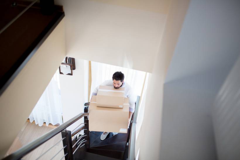 how much does decluttering cost - Man carrying cardboard boxes up a staircase
