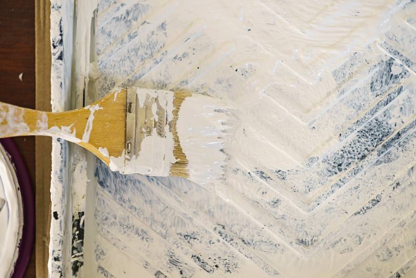 how to limewash walls - Paintbrush applying white coating over textured wall surface