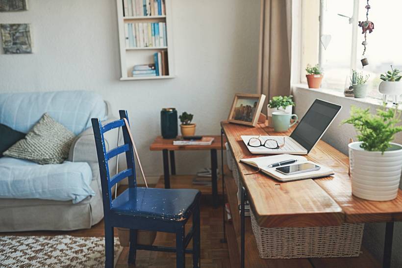 professional organiser cost - Bright living room workspace with wooden desk, laptop, notebooks, and potted plants