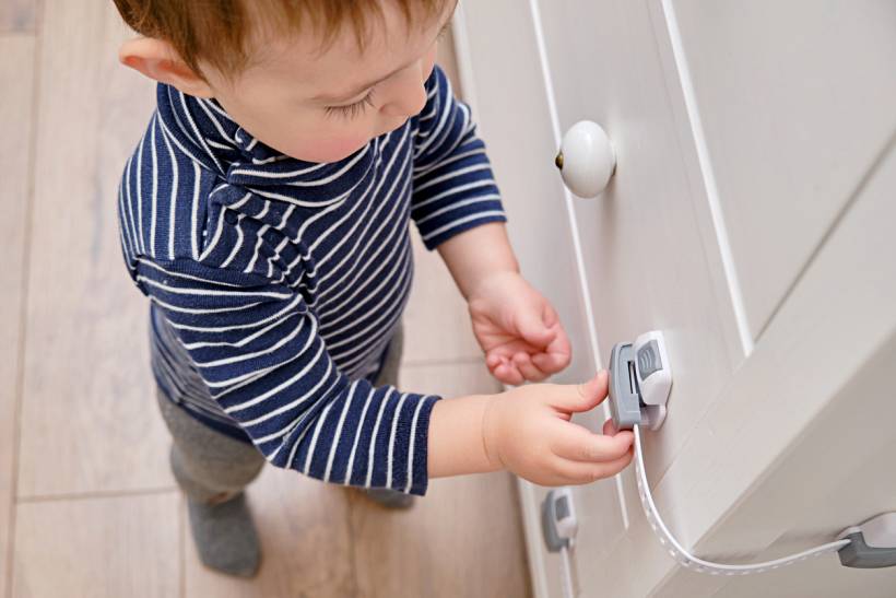 professional organiser cost - Toddler reaching for child safety lock on white cabinet door
