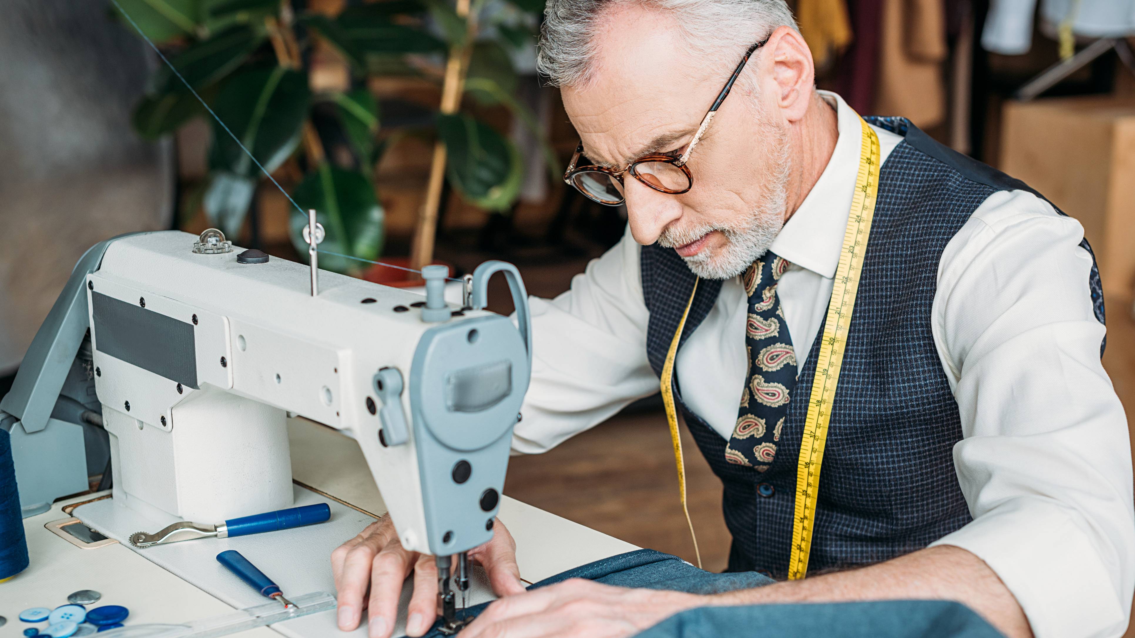 Handsome tailor in glasses using a sewing machine