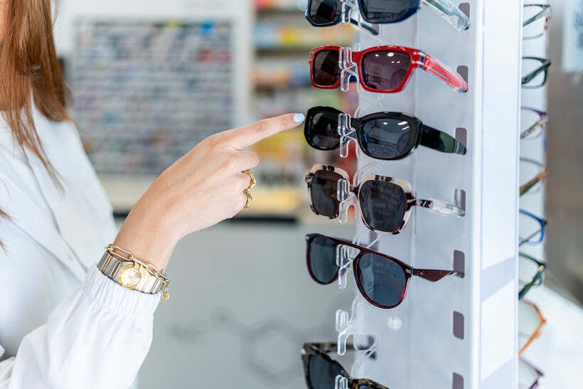 A hand pointing to sunglasses arranged on a retail display stand. - retail tasks