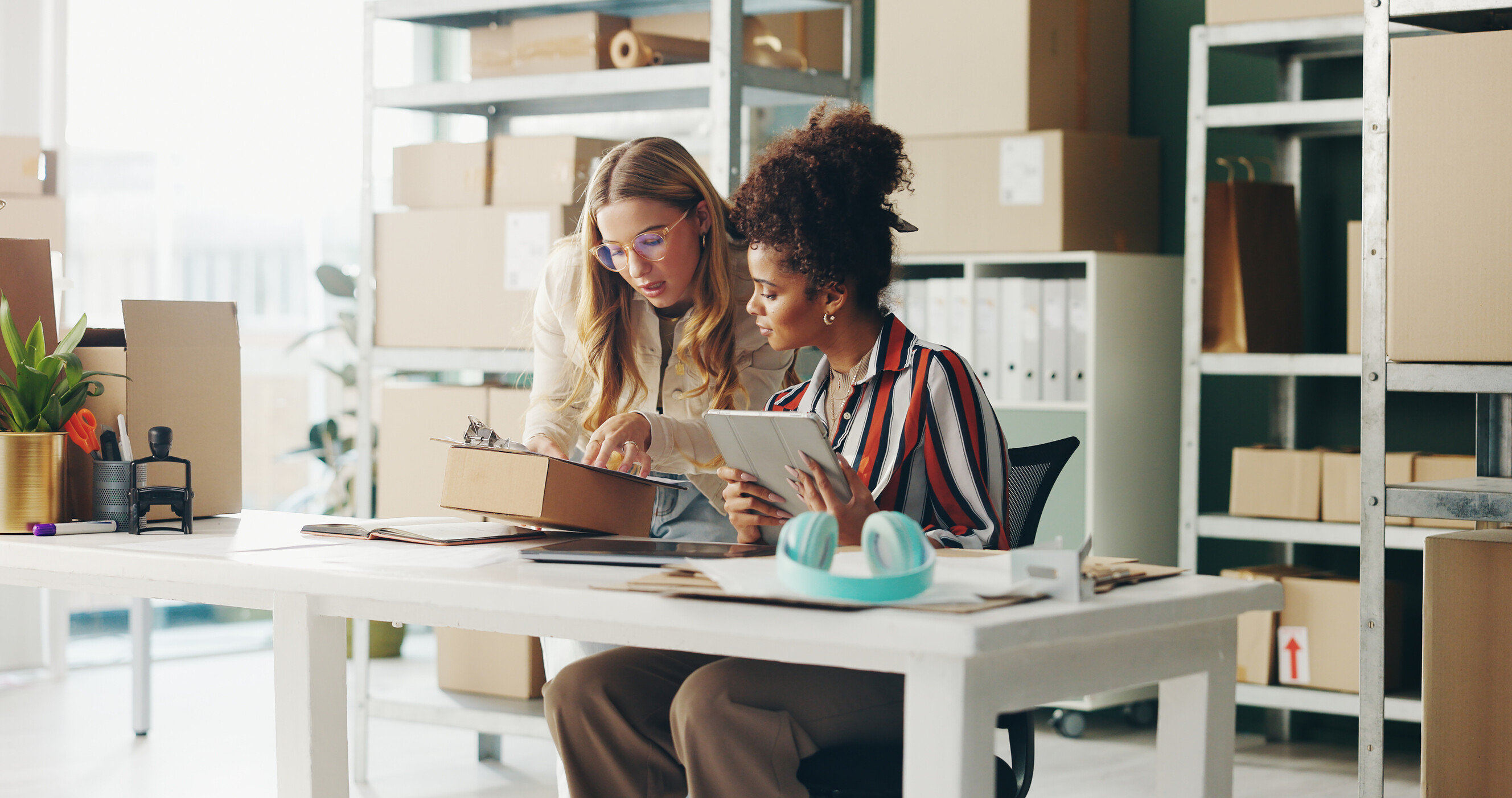 Two colleagues collaborating over a tablet while managing online order packages.