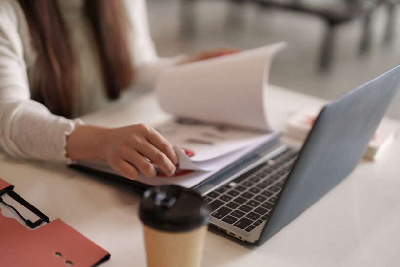 A woman reviewing business documents next to a laptop at her desk. - ecommerce tasks