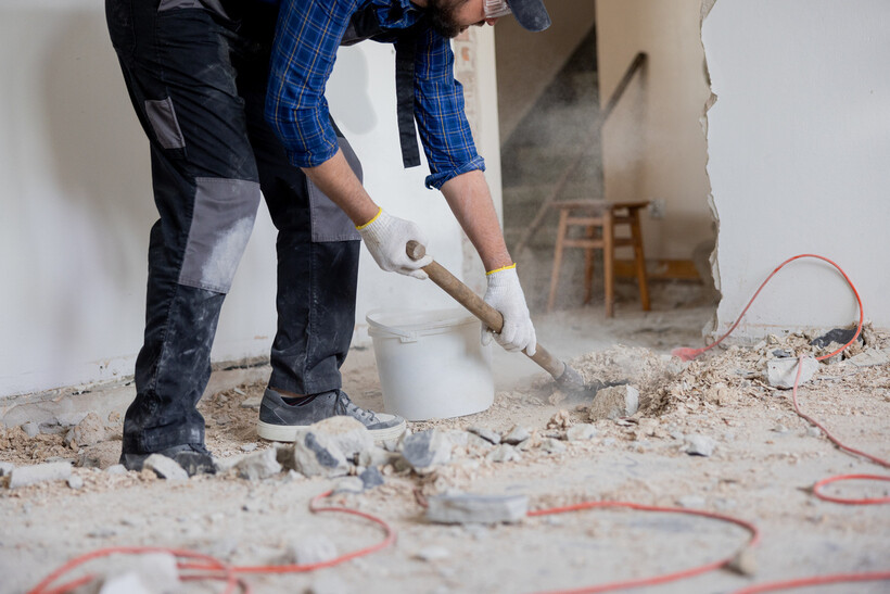 Legs and shovel of a protective-gear-clad worker clearing debris from a construction site. - after builders cleaning