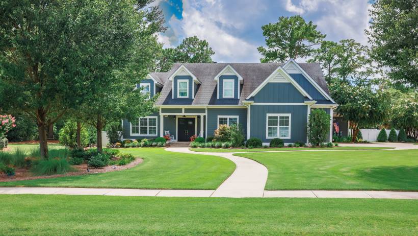Front yard view of a large suburban home featuring a lush green lawn, mature trees, and curated landscaping. - crabgrass removal
