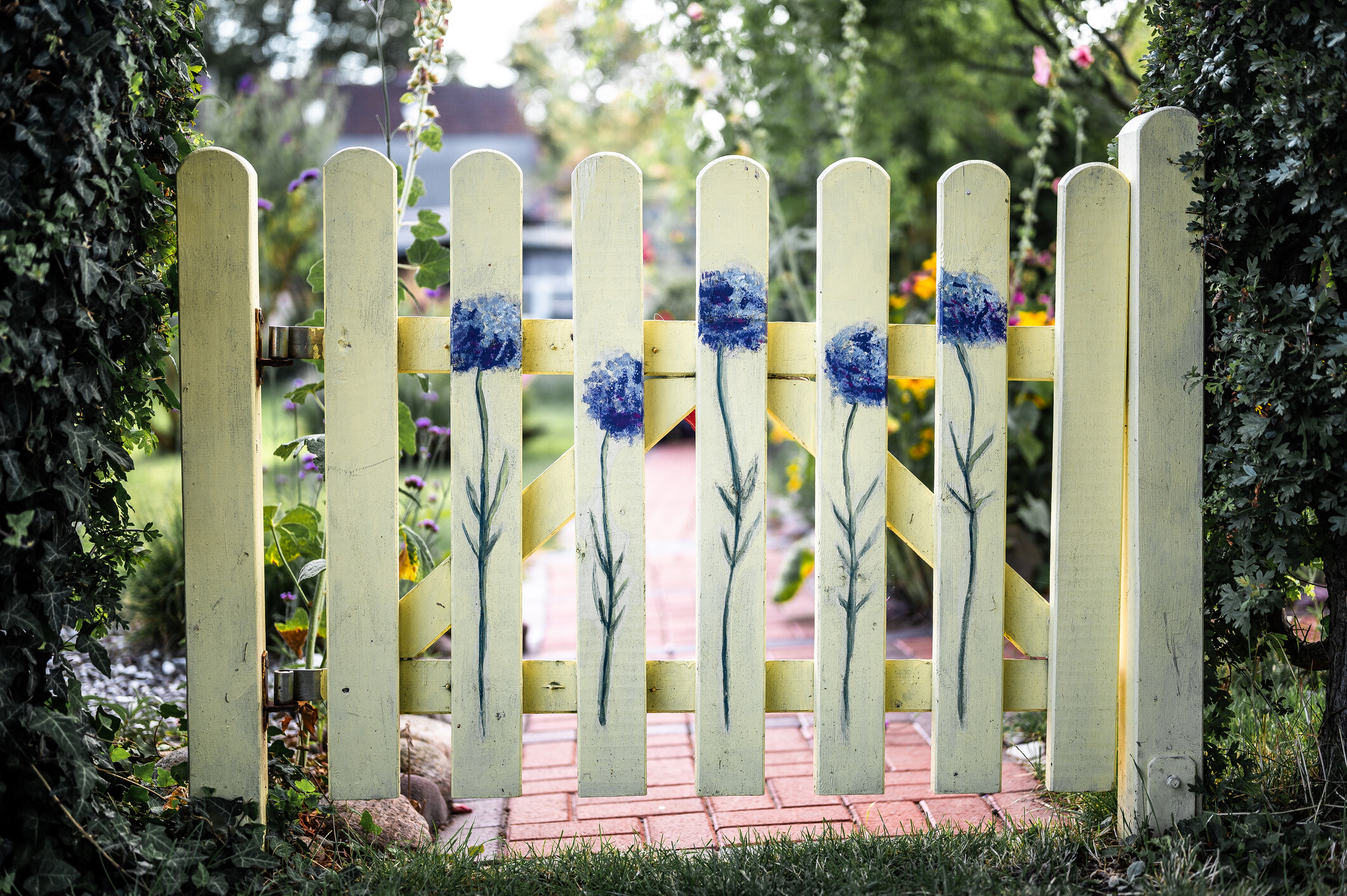An outdoor path framed by a cream-coloured fence gate painted with detailed flower art. - garden fencing cost