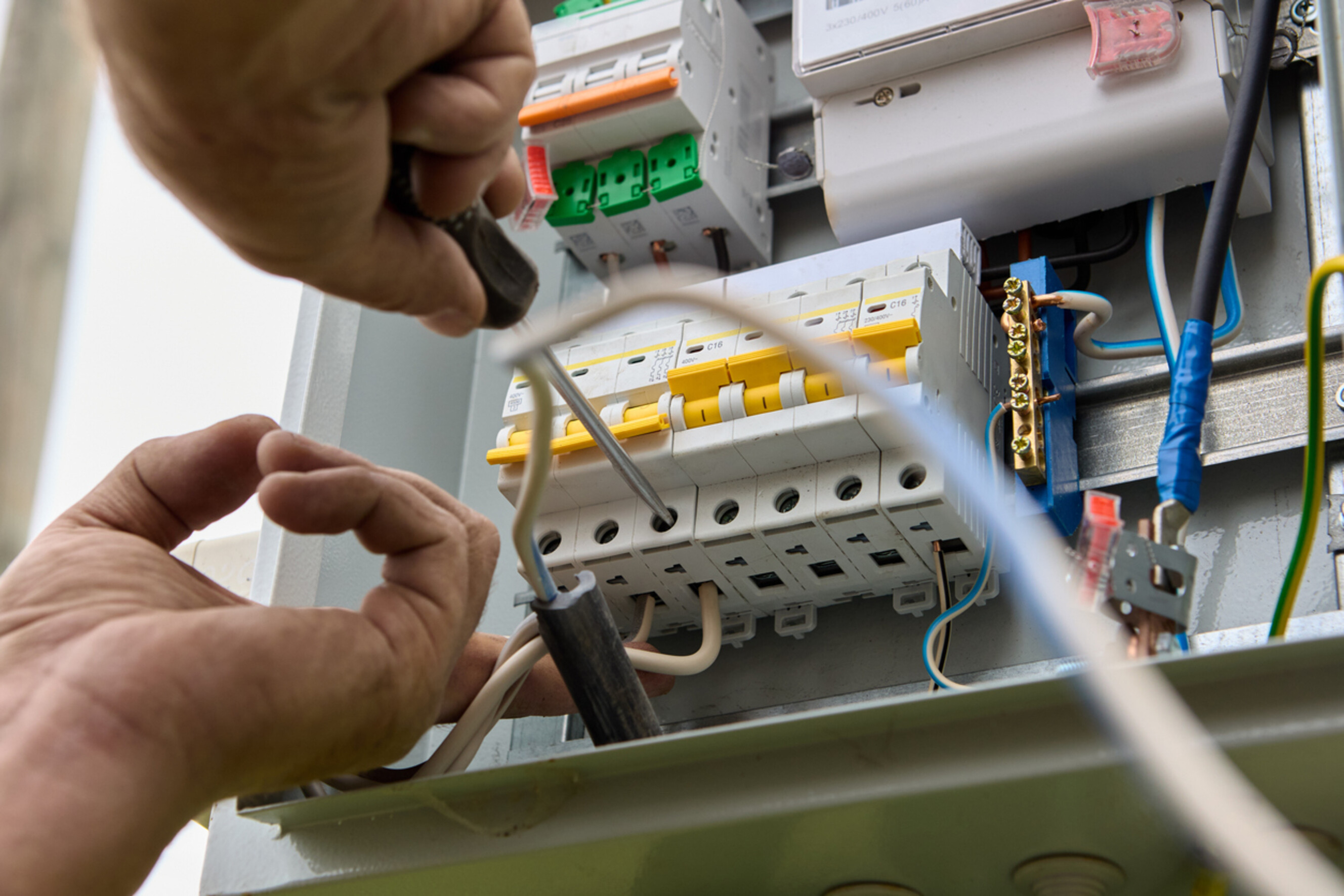 A person mounting circuit breakers inside a home switchboard panel.