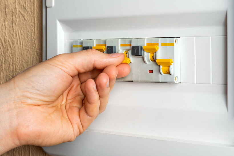 Person flicking an RCD switch to the on position in an electrical panel. - how to use switchboard