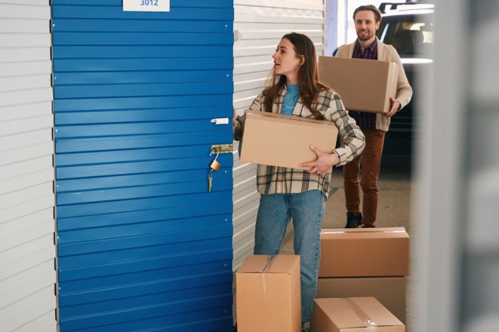 A woman holding a large cardboard box and opening the door to the self-storage warehouse.
